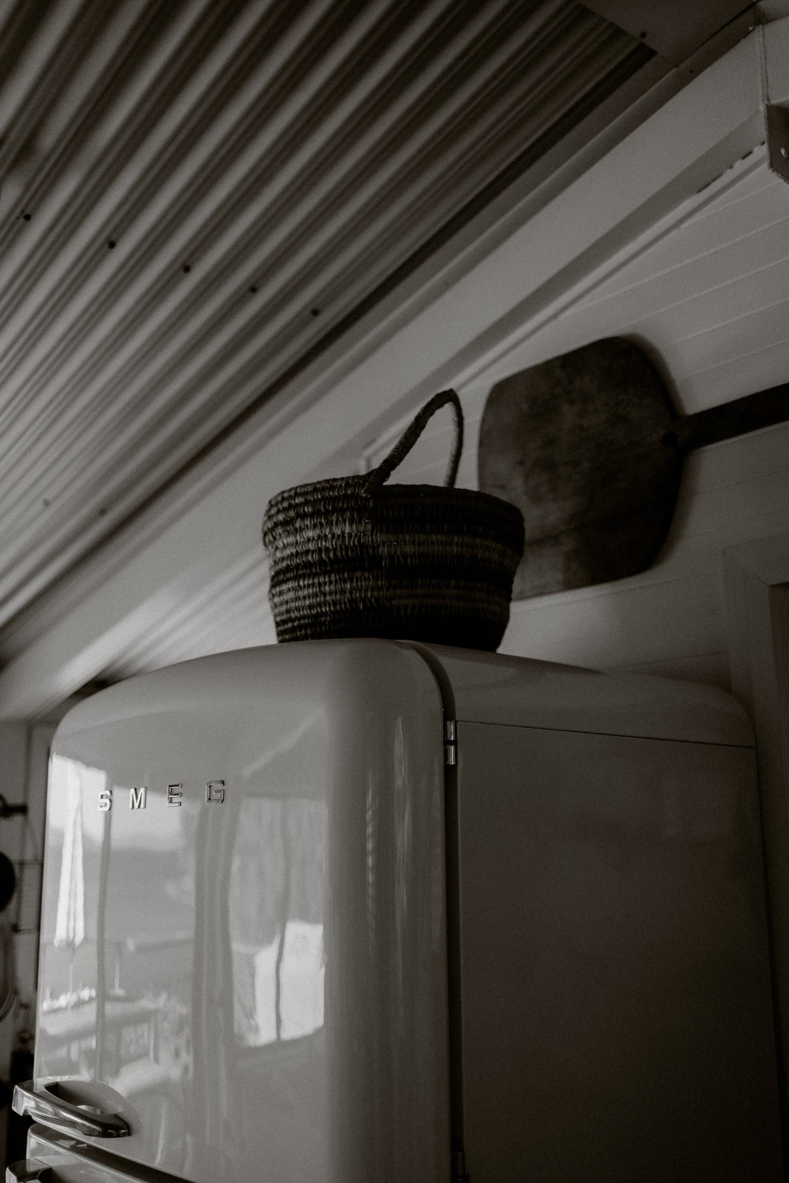 Cream retro fridge with a woven basket resting on top, against a panelled wall