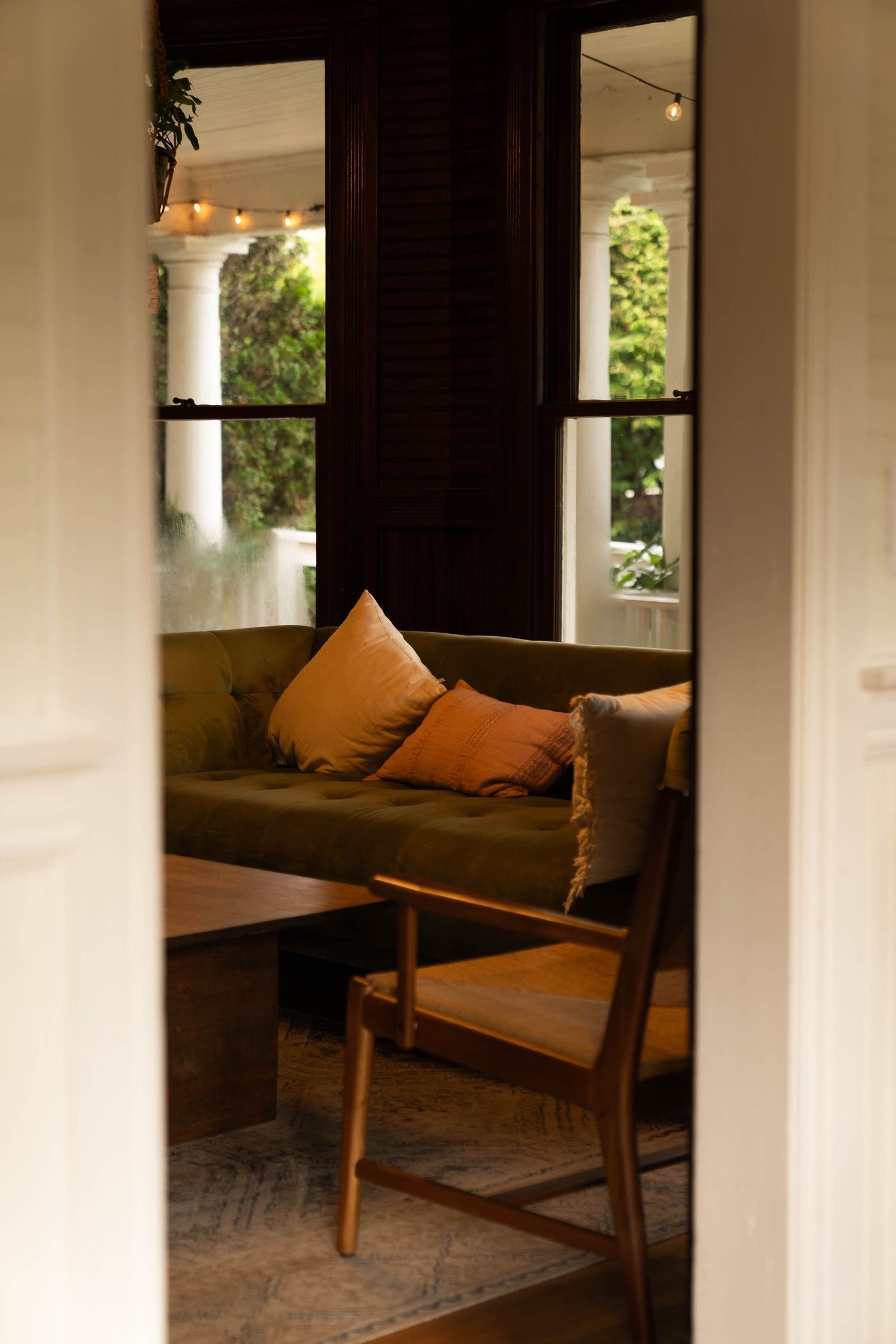 Olive green sofa with rust-toned cushions, seen through an open doorway