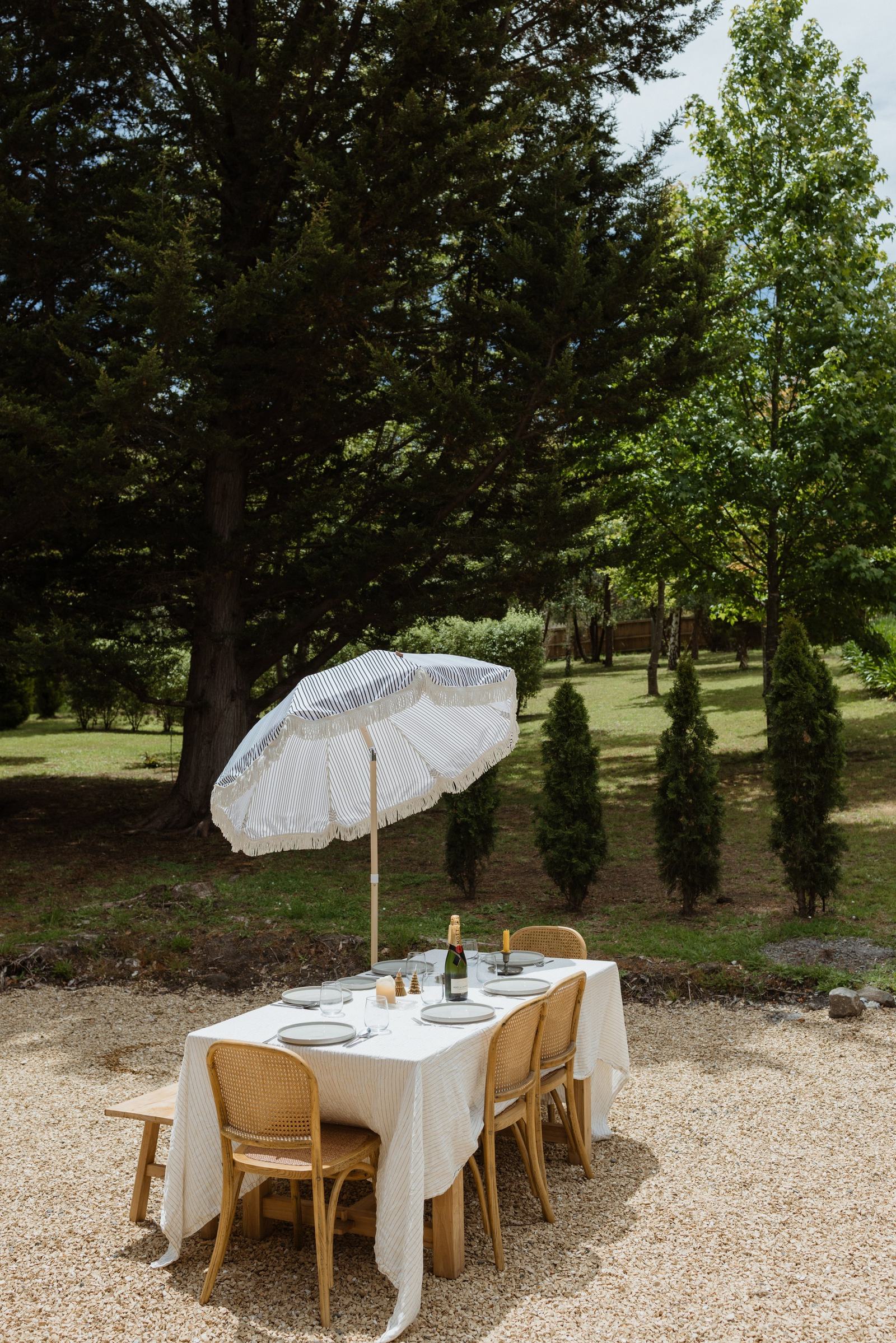 White fringed garden umbrella shading an outdoor setting on a lawn surrounded by trees